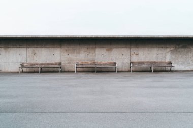 Metal ayaklı grunge beton duvar büyük bir boş alan ön planda tek bir şerit ile Asfalt Küçük delikli önünde duran üç Ahşap banklar geniş açı minimalist atış