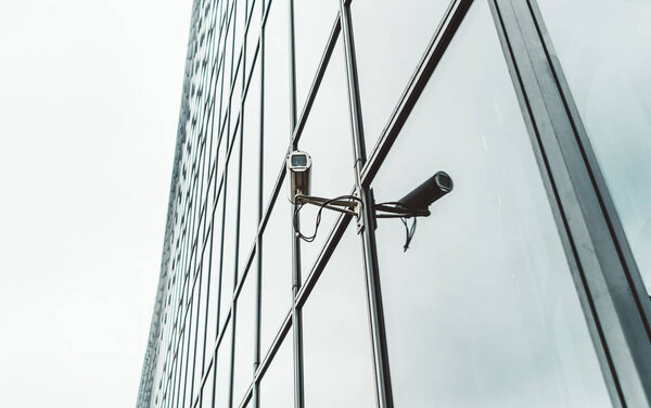 Close-up view of a contemporary surveillance video cam attached to the facade of a modern business skyscraper; security video camera on the frontage of an office high-rise