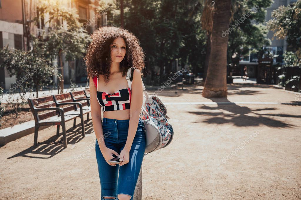 Young dreamy curly female tourist is leaning against a small pillar on the street of Barcelona and wistfully looking up with copy space place for your logo or a text messgage