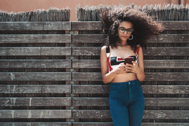 Sevimli genç biracial erkek wattle Çitten içeri ile ahşap bir çit karşı yaslanmış ve onun smartphone, gelen mesajları bir kopya yer alan metin veya logo için soldaki ile kontrol