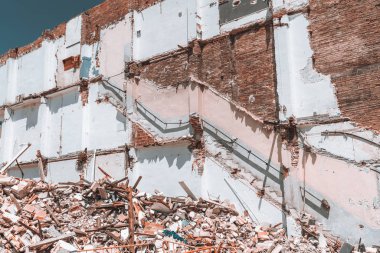 Bir tuğla duvar kısmen yıkılan evin yıkım çalışmaları sırasında görünümünü: korkuluk duvar, sıva, kısmen yırtılmış sıva, inşaat atıkları önde, yığınları güneşli bir gün