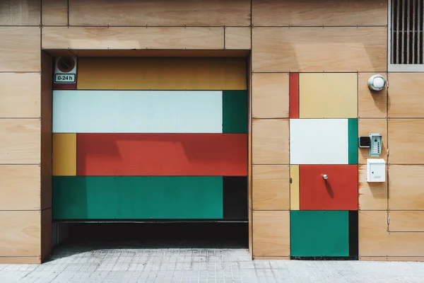 Multicolored fancy wooden facade of an ordinary house on a street of Barcelona: partly opened garage door, smaller entrance door with intercom and mailbox near — Stock Image Multicolored Fancy Wooden Facade Ordinary House Street Barcelona Partly Opened Stock Picture