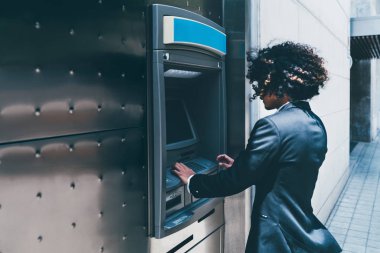 Yan görünüm açık bir Atm kullanarak onun banka kartından para çekme bir işadamı; kıvırcık adam girişimci otomatik vezne makinesi için sokakta onun hesabına depozito doldurmak için kullanıyor