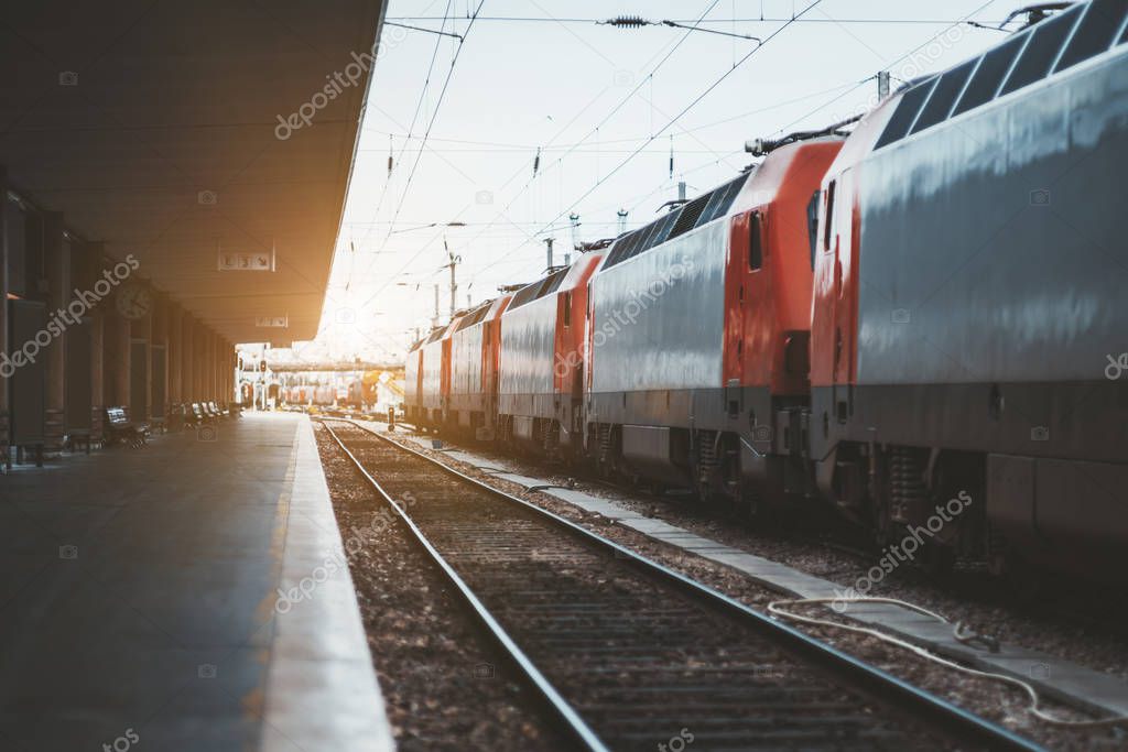 The railroad platform with one empty track and a train consisting of locomotives of red and grey colors on other track, Lisbon, Portugal, shallow depth of field
