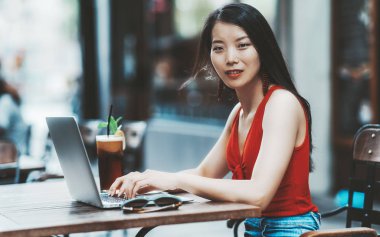 Neşeli Genç Asyalı kadın açık bir barda onu laptop kullanıyor; uzun siyah saçlı Asyalı kız sevimli sokak kafe, lezzetli içecek nane onun yanındaki ile onun netbook ile çalışma