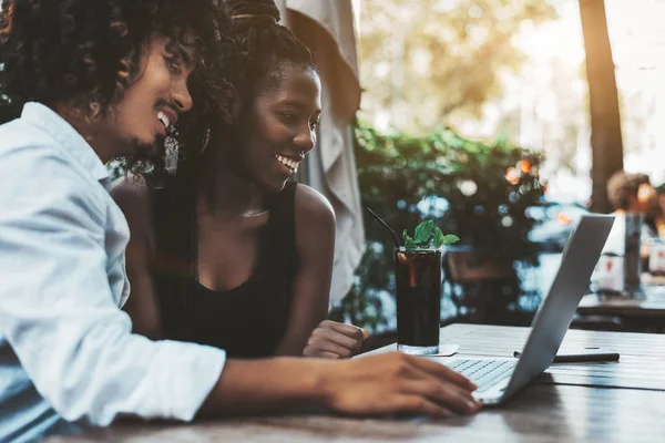 Mutlu bir ırklararası çift: Asyalı bir adam ve siyah bir kız sokak bir kafede kahvaltı ve onların laptop, lezzetli nane masaya kokteyl cam ekran bir film izlerken