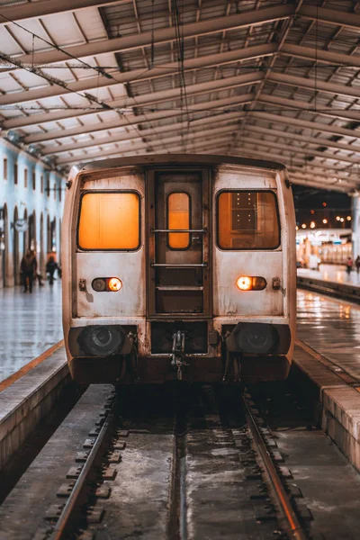 A vertical frontal view of a grungy locomotive cabin indoors of a train station depot during maintenance; night railway station platform with a suburban carriage waiting for the boarding, Lisbon