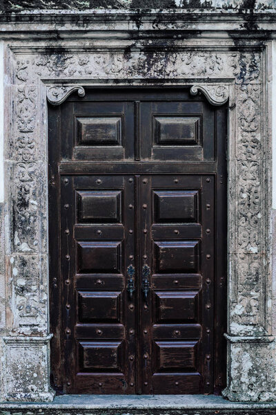 Vertical shot of a huge antique refined wooden door in a stone wall with bas-relief, Sintra, Portugal