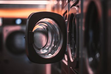 Karanlık bir odada birden fazla çamaşır makineleri içinde açık kapı sığ derinlik-in tarla, güçlü bokeh bir çamaşır kurutma makinesi, tarih seçici odak ile ortak bir çamaşır