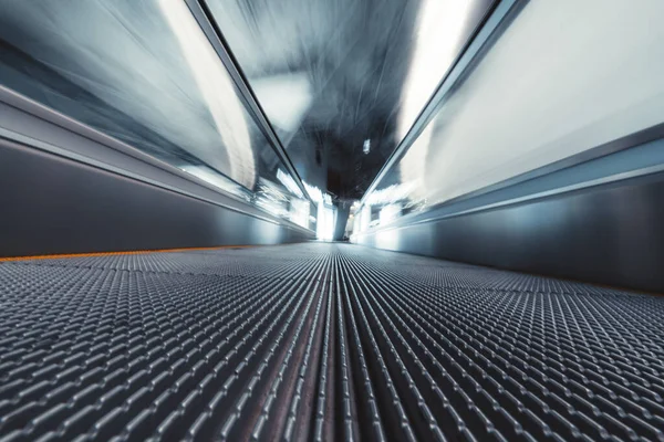 Long exposure shooting from the bottom of a moving walkway in an airport terminal; travelator through contemporary departure area of railway station depot with stretching to the vanishing point