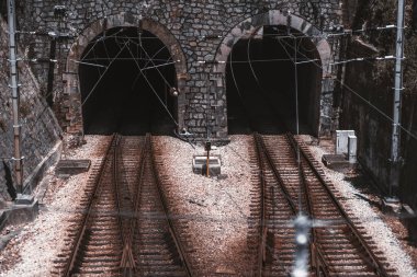 Önünde demiryolu kavşakları ve kenarlarında elektrik kabloları olan, güneşli bir günde, yerde çakıl taşı, Sintra, Portekiz 'de, karanlık demiryolu tünelleri ve taş duvarlardan oluşan iki giriş.