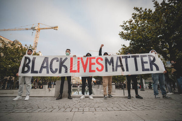 Porto, Portugal - June 6, 2020: demonstration against racial discrimination: a group of six African and mixed men protesters holding a huge banner with a text "Black lives matter" on the street
