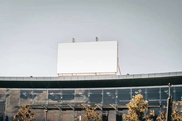 An empty huge poster mockup on the roof of a mall; white template placeholder of an advertising billboard on the rooftop of a modern building with glass facade; blank mock-up of an outdoor ad banner