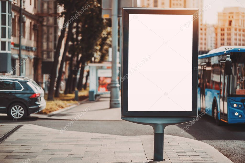 A city empty urban billboard mockup for an advertising and a blue bus passing by; the template of clean urban information banner placeholder on a pavement, with a trolleybus near it on the road