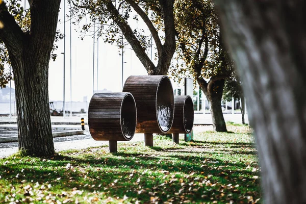 View with a shallow depth of field of three benches of unusual round shape with lathing outside and lacquered metal inside mounted in the shadow of trees of an autumn public park in Belem, Lisbon