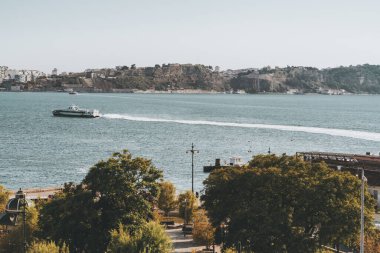 Önünde bir parkın ağaçları ve arka planında bir uçurum bankası olan Tagus, Lizbon 'dan geçen ve geride uzun bir iz bırakan bir nehir ve yolcu teknesi olan güzel bir manzara.