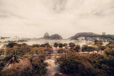 Rio de Janeiro, Brezilya 'nın Botafogo bölgesinin geniş açılı drone görüntüsü; ön planda birden fazla palmiye ve diğer tropikal ağaçlar, uzaklarda yelkenli tekneleri olan bir körfez ve Sugar Loaf tepeleri bulunuyor.