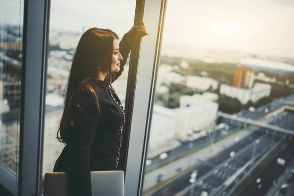一个成熟的迷人的加尺寸的高加索女企业家的画像 靠着商业大厦顶层的窗梁 手持笔记本电脑 凝视着下面的高速公路 — 图库照片