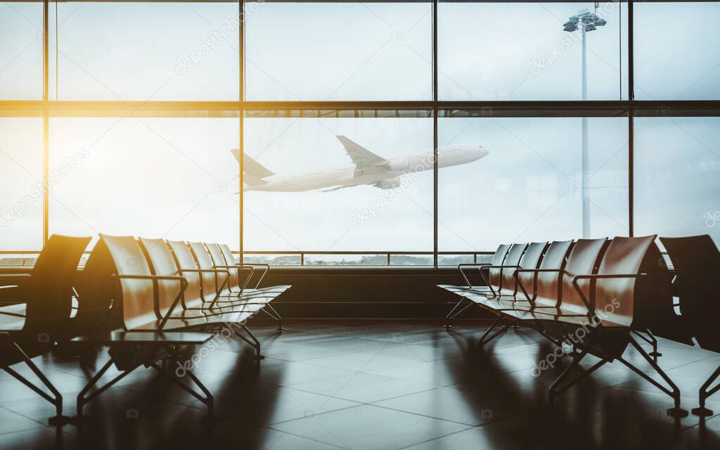 An empty waiting hall of a contemporary airport with empty rows of seats during lockdown and quarantine without passengers and with a single airplane taking off and gaining altitude outside the window