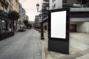 Klasik ve modern binalarla çevrili sessiz bir yaya caddesinde boş beyaz ekranlı dikey şehir reklam panosu modeli, kentsel reklamcılık veya markalaşma görselleri için mükemmel.