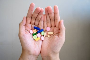 Eczacılık ürünleri ve refah üzerine yoğunlaşarak, bir kişinin çeşitli renkli ilaç ve kapsüllerden oluşan bir koleksiyonu tutarken, sağlık, tedavi ve ilaç kullanımını gösteren yukarıdan aşağıya bir bakış.