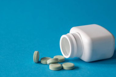 Mavi arka planda ilaç paketi, masada haplar.