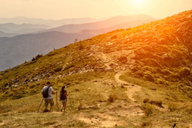 Bir adam ve bir kadın dağlarda yürüyorlar.