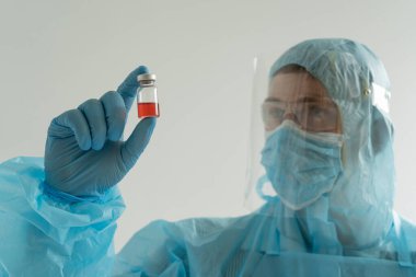 Koruyucu kıyafetli doktor ilacı elinde tutuyor, bir aşı.