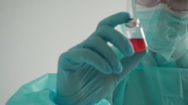 İlaç geliştirme süreci, koruyucu giysili bir doktor ampul tutuyor.