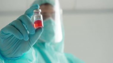 İlaç geliştirme süreci, koruyucu giysili bir doktor ampul tutuyor.