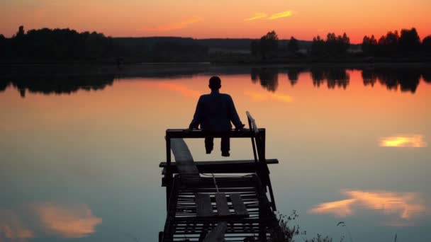 Расслабляясь на озере, парень наслаждается закатом на озере — стоковое видео