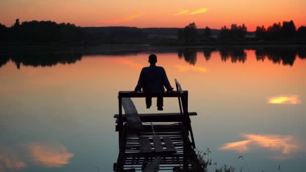 Relaxing on the lake, the guy is enjoying the sunset on the lake — Wideo stockowe