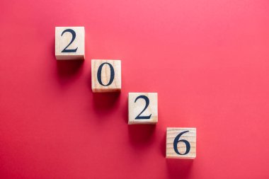 Ahşap bloklardaki 2026 numara kırmızı zemin üzerinde çapraz hizalanmış, yatay yön ve tek ışık. Uzayı kopyala Takvim ve gelecekteki hedefler kavramı