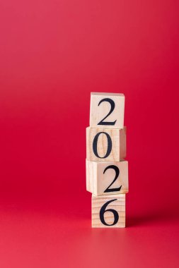 Ahşap bloklar dikey olarak düzensiz bir şekilde istiflenmiş ve 2026 'yı oluşturmuş, parlak kırmızı bir zemin üzerinde. Kopyalama alanı olan dikey biçim. Yeni yıl ve gelecek planlama kavramı