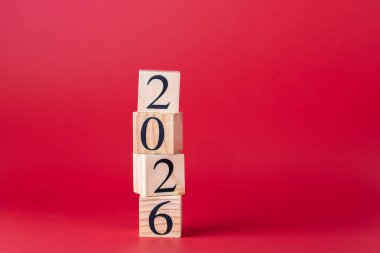 Yanlış hizalanmış ahşap bloklar 2026 sayısını oluşturarak kırmızı zemin üzerine yerleştirildi. Kopya uzayı ile yatay formatta temiz kompozisyon. Yeni yıl ve iş hedefleri kavramı