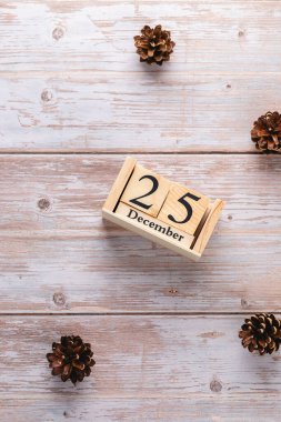 Tahta bloklar takvimi 25 Aralık 'ı gösteriyor, açık ahşap masaya konmuş, doğal çam kozalakları etrafa saçılmış. Kopyalama alanı olan minimalist dikey düzen. Noel ruhu ve şenlik havası kavramı