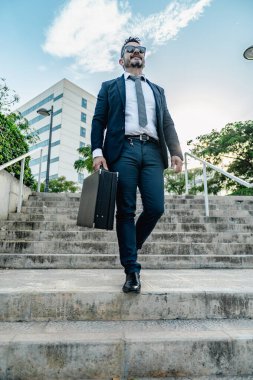 Profesyonel takım elbiseli ve güneş gözlüklü adam şehir merdivenlerinden güvenli bir şekilde iniyor.
