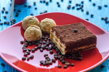 Kırmızı bir tabakta tiramisu keki, bir fincan kahvenin yanında, açık ahşap bir arka planda fotoğraflanmış..