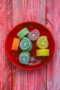 Kırmızı bir tabakta kırmızı bir tahta sırtında çok renkli marmelat.