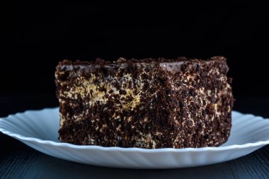 Bir parça çikolatalı kek, beyaz bir tabakta, siyah bir tahta sırtında.