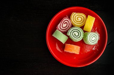 Siyah ahşap bir sırt deliğinde kırmızı bir tabakta çok renkli marmelat.