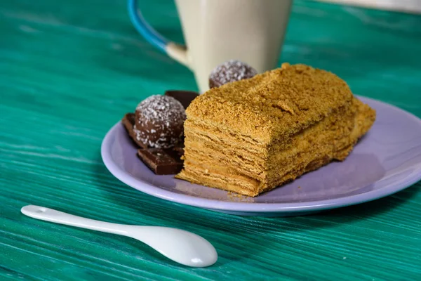 Bir parça kek ve bir tabakta çikolata, yanında bir fincan kahve, yeşil ahşap bir arka planda yakın plan fotoğrafı..