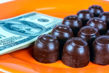 Turuncu bir tabağın üstünde çikolatalı şekerler ve nakit parayla.