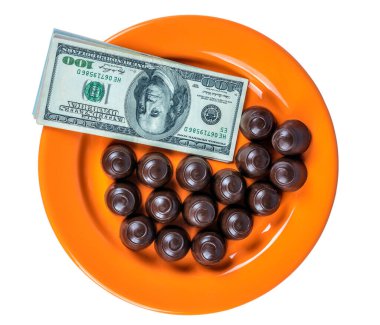 Turuncu bir tabağın üstünde çikolatalı şekerler ve nakit parayla.