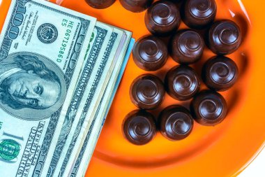 Turuncu bir tabağın üstünde çikolatalı şekerler ve nakit parayla.