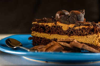 Turkuaz seramik bir tabakta, siyah ahşap bir fonda, bir fincan kahvenin yanında Tiramesu keki..