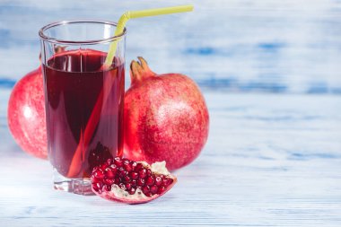 Tahta zemin üzerinde nar suyu ve nar meyveleriyle dolu cam deney şişesi.