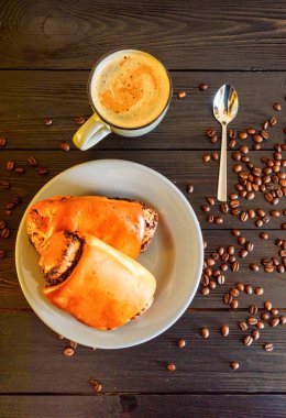 Gri tabakta haşhaş tohumlu çörekler ve siyah ahşap arka planda kahve kupası. Kahve çekirdeğinin yanında.