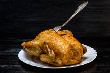 Beyaz tabakta kızarmış tavuk, siyah ahşap arka planda.
