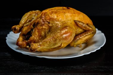 Beyaz tabakta kızarmış tavuk, siyah ahşap arka planda.